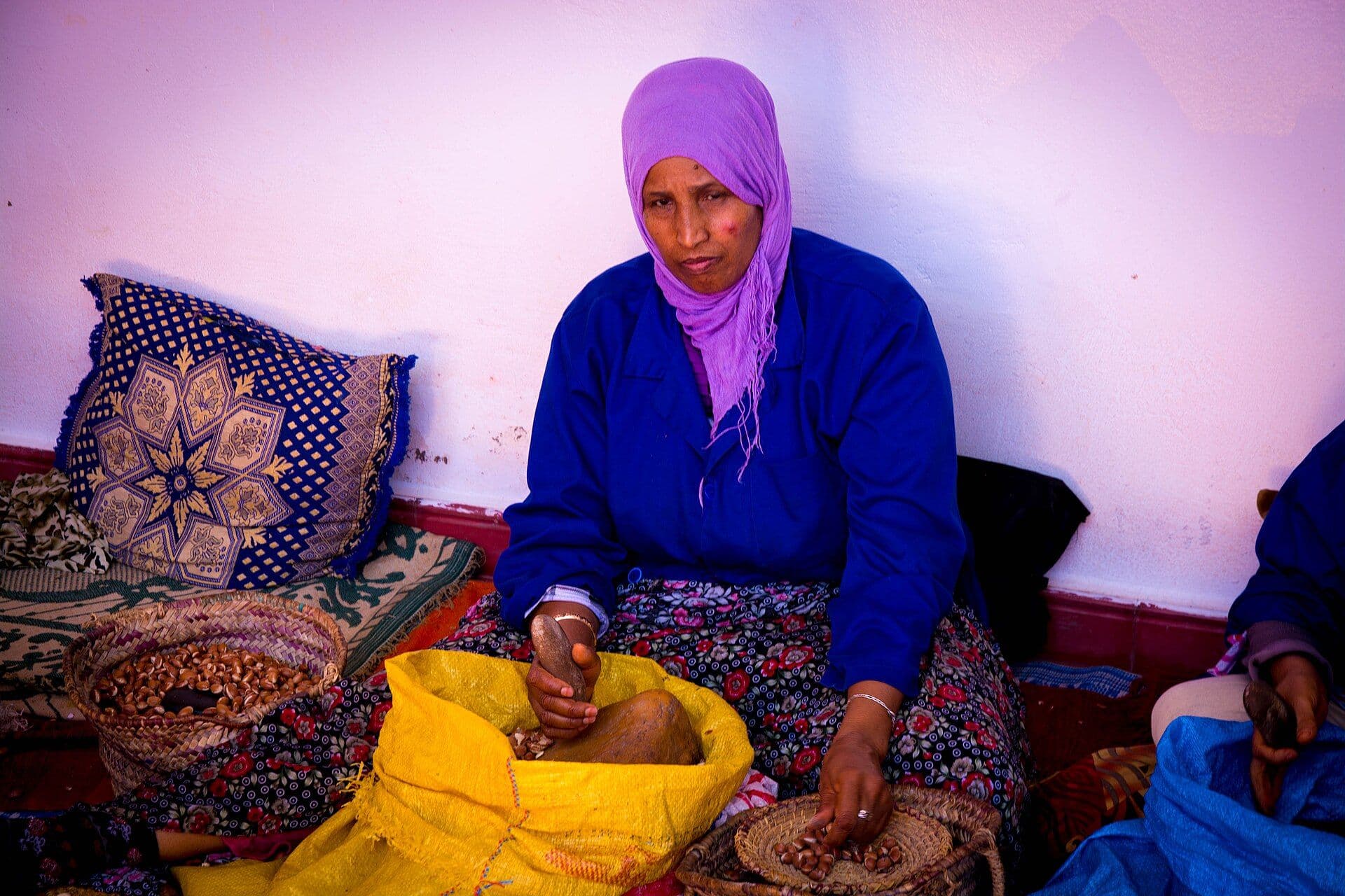Moroccan woman in a colorful headscarf cracking argan nuts at a cooperative