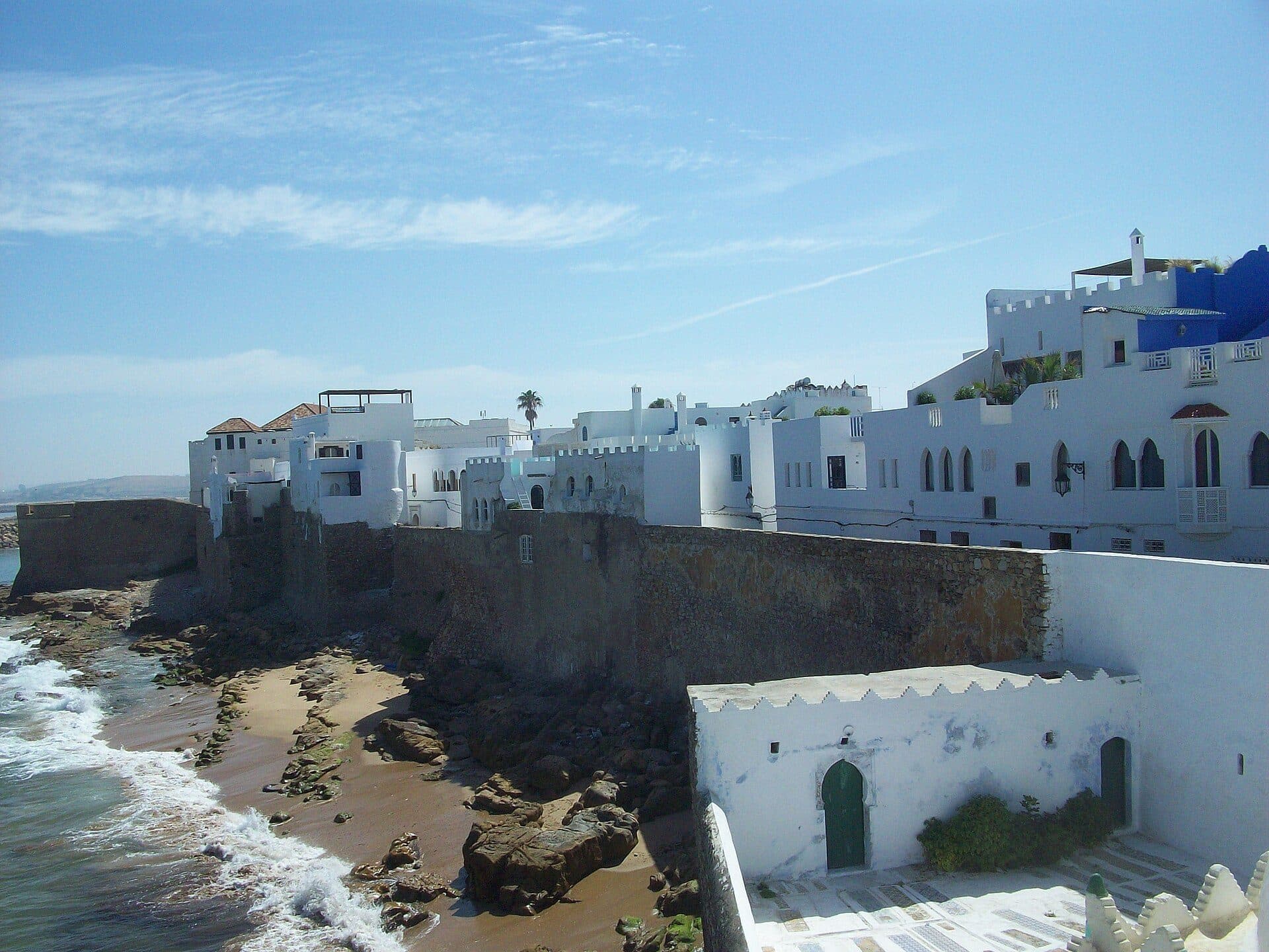 White houses above the old town wall of Asilah, with a small beach and waves at its foot