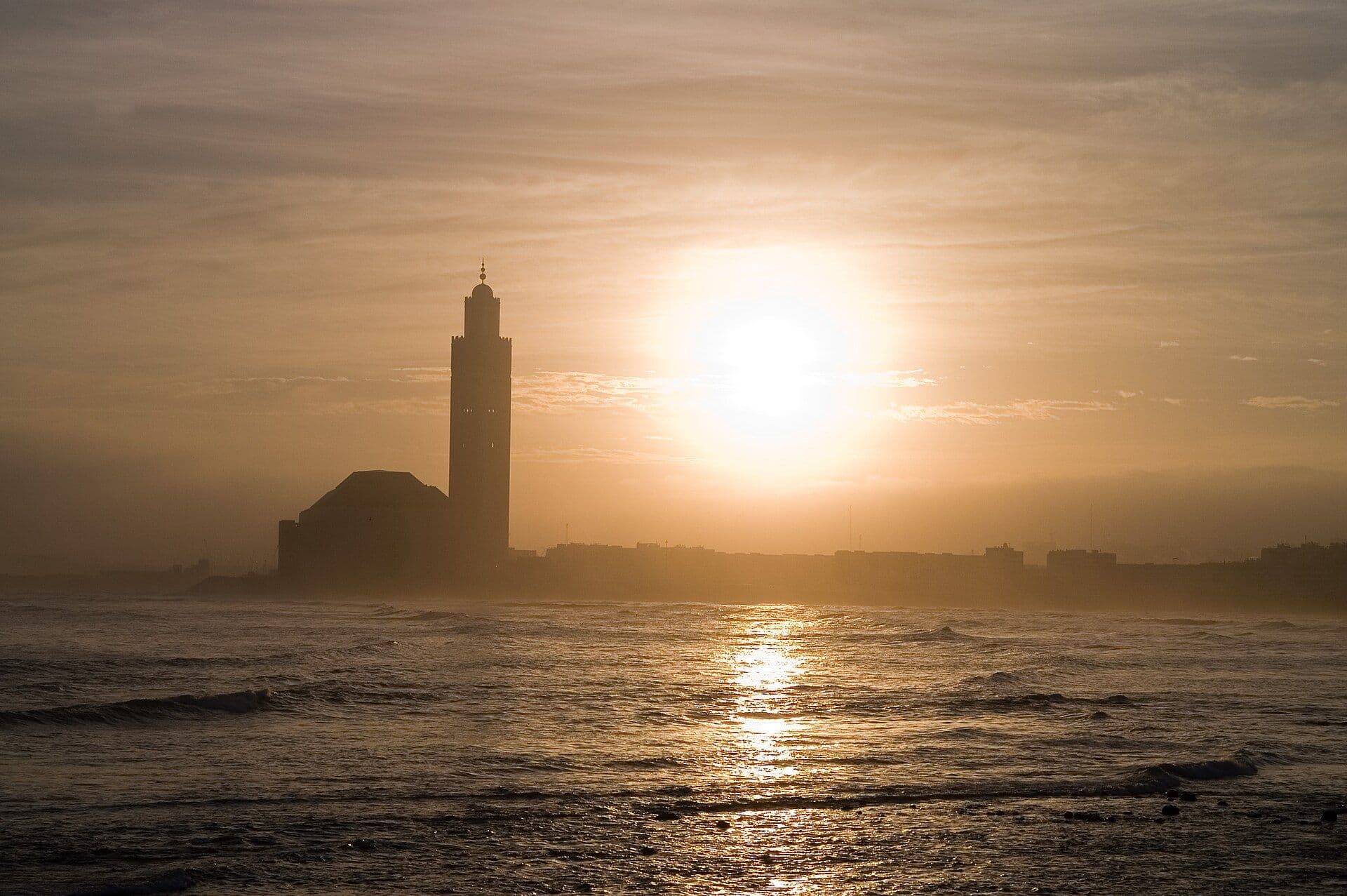 The silhouette of the Hassan II Mosque in Casablanca against the sunset over the ocean