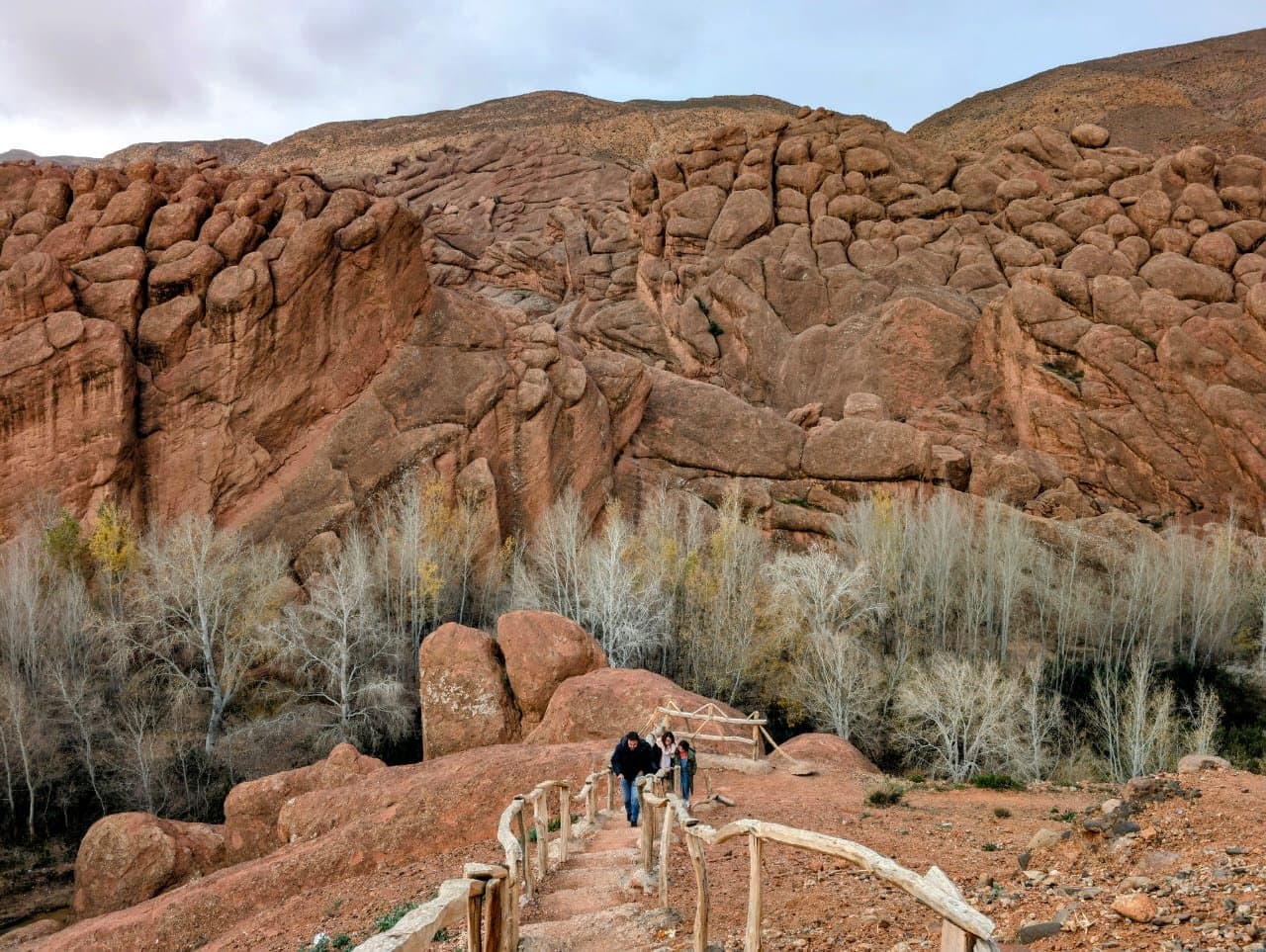 A path with a wooden railing between round, eroded rocks in the Dadès Valley, with two walkers