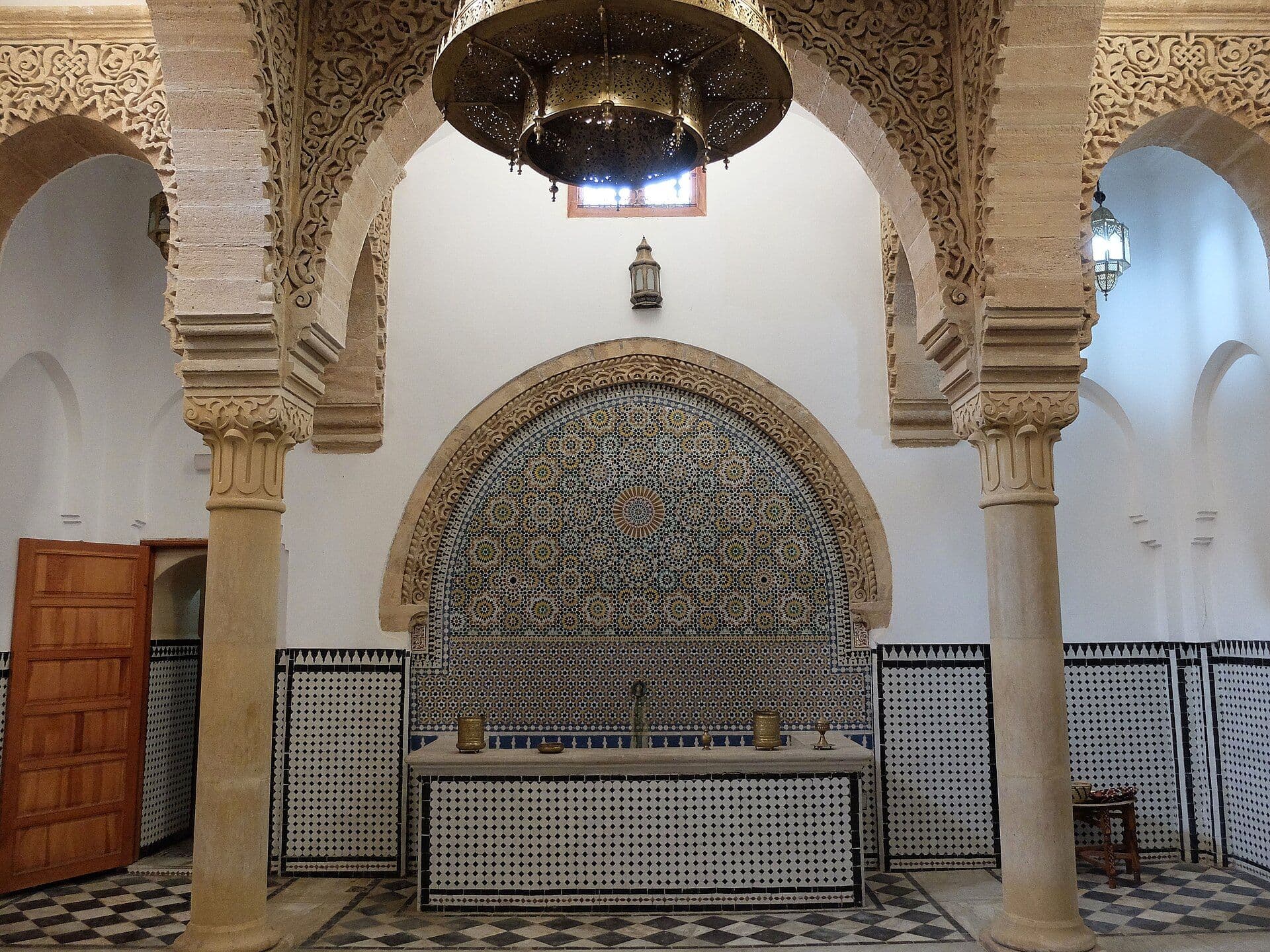 Interior of a traditional hammam with arches, zellige tiles and a copper lamp