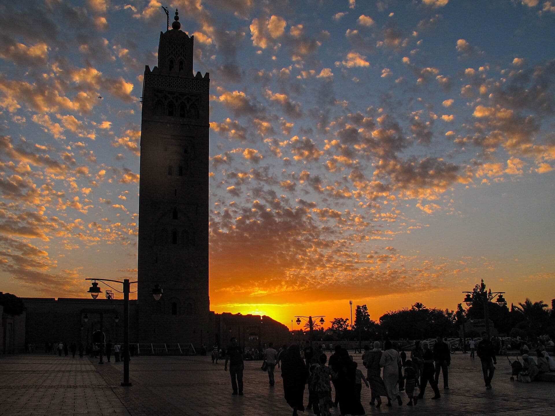 The Koutoubia minaret in Marrakesh at sunset, with people strolling on the square in front of it