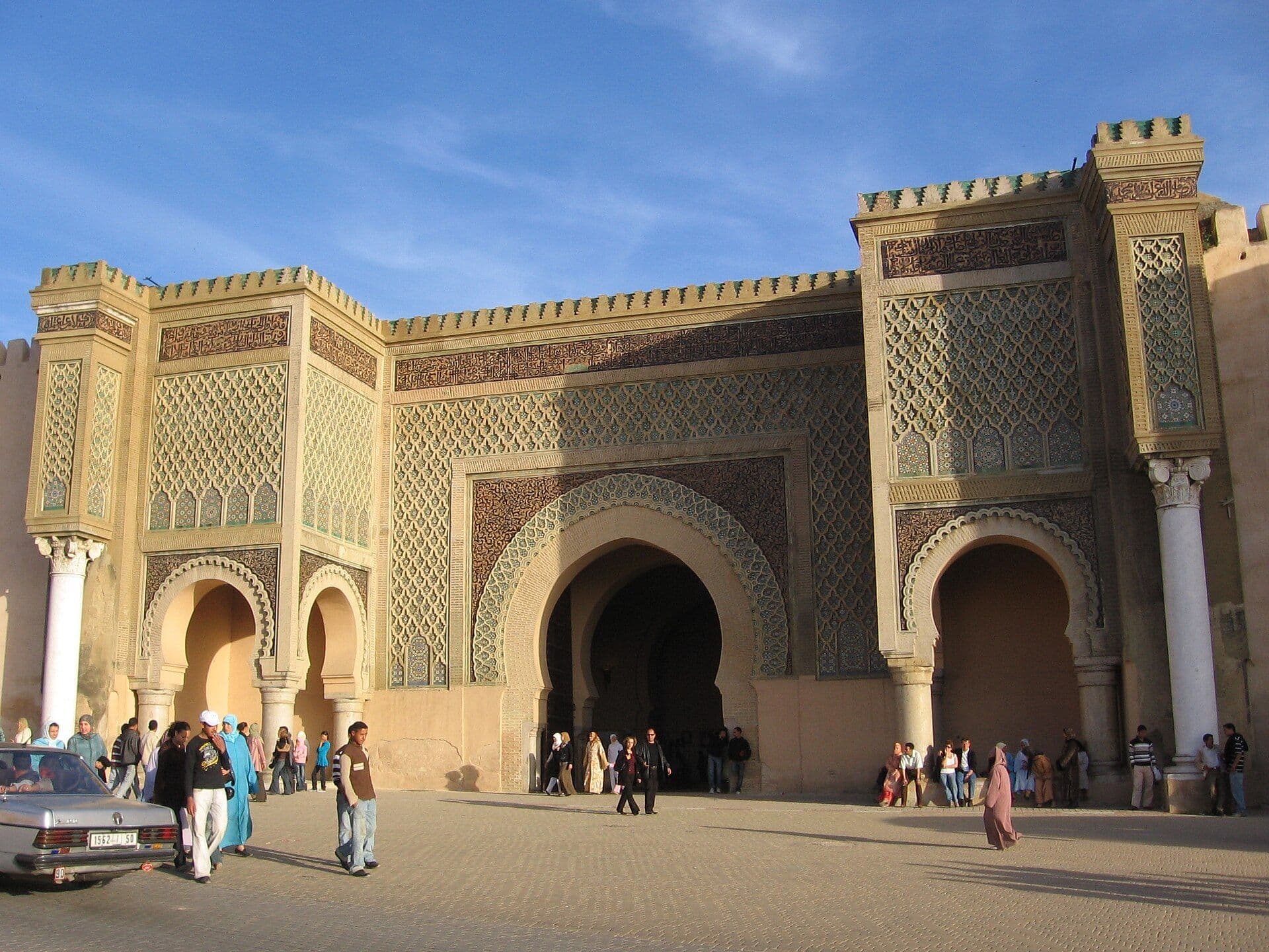 The large decorated Bab Mansour gate in Meknes with people on the square in front of it