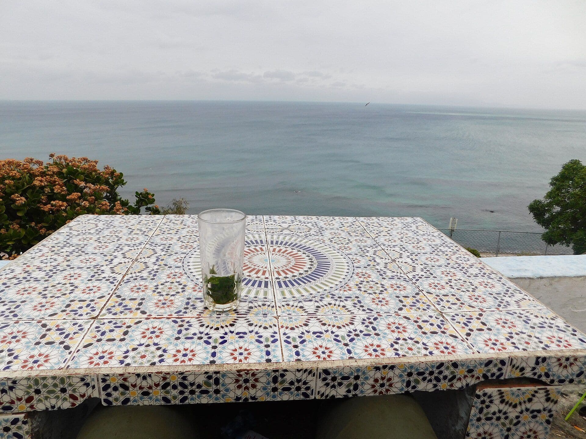 A glass of mint tea on a table with zellige tiles and a view of the sea