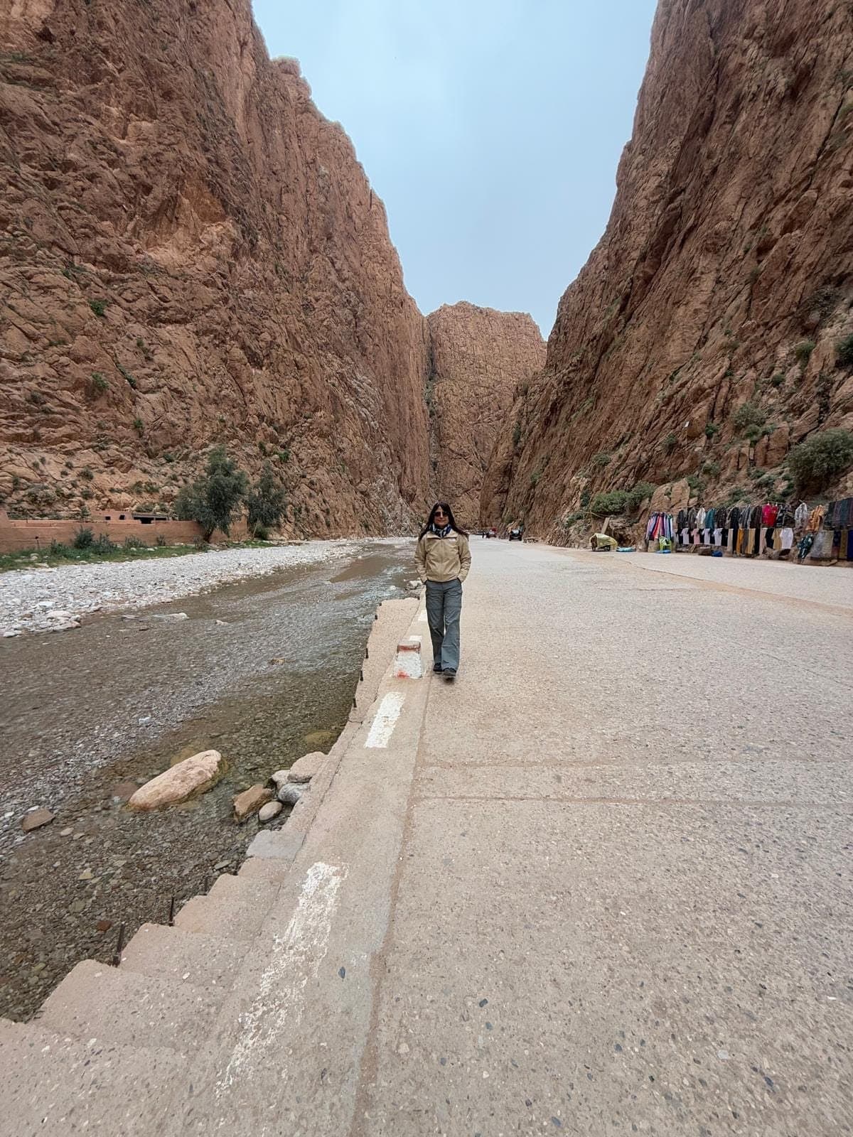 Someone walks on the path along the stream in the Todra Gorge, between tall rock walls